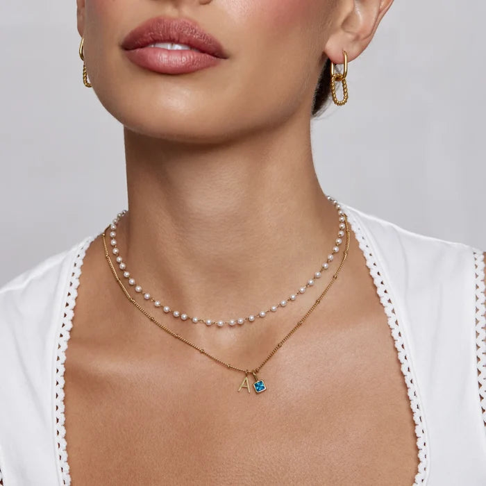 Model wearing Gem Initial Necklace with letter A and blue birthstone layered with pearls
