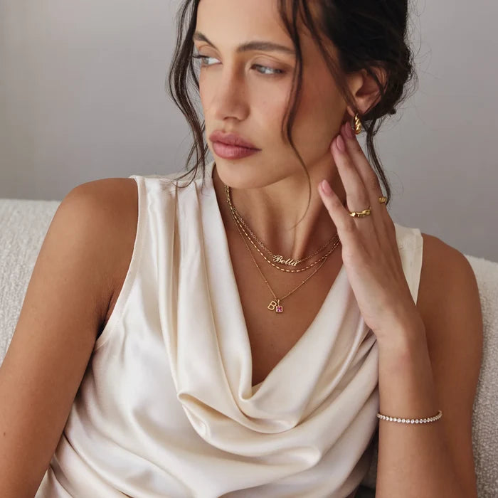 Gem Initial Necklace layered with Bella name necklace and gold chains on model