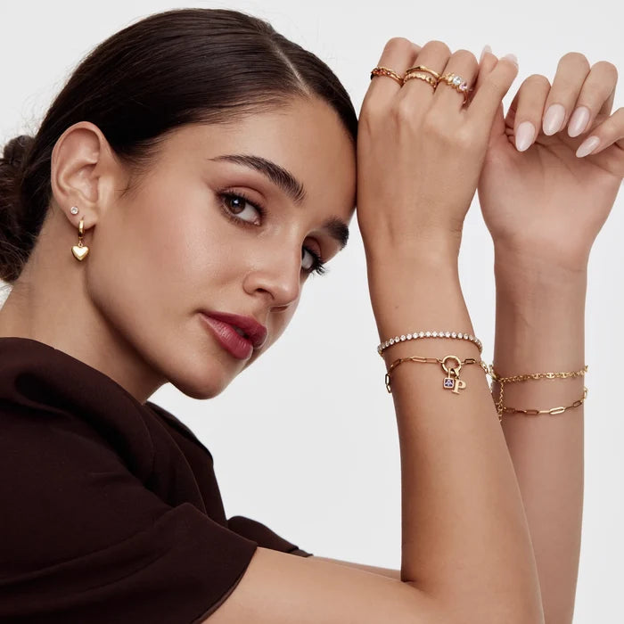 Model wearing stacked gold bracelets including Paperclip Initial Birthstone Bracelet